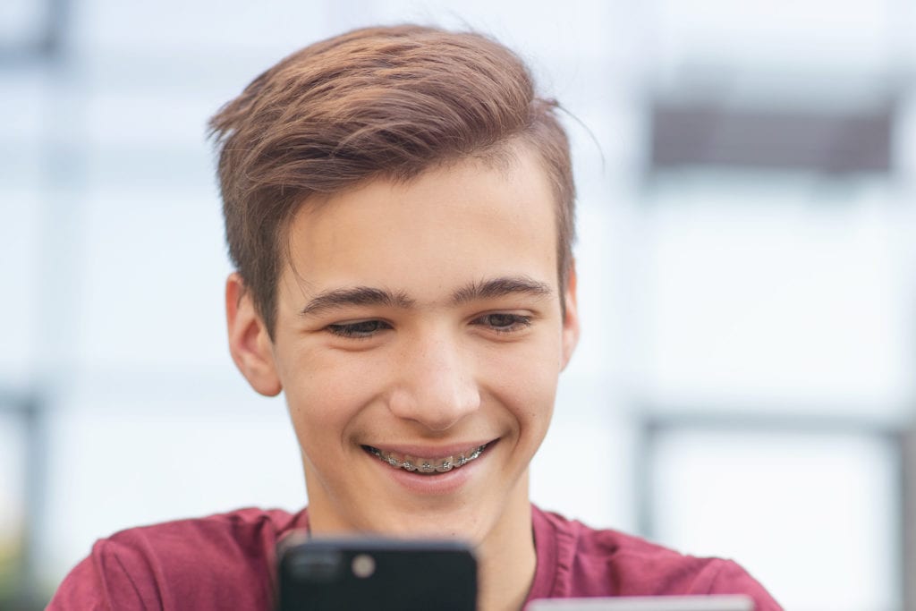 Smiling teenage boy in braces playing on his phone