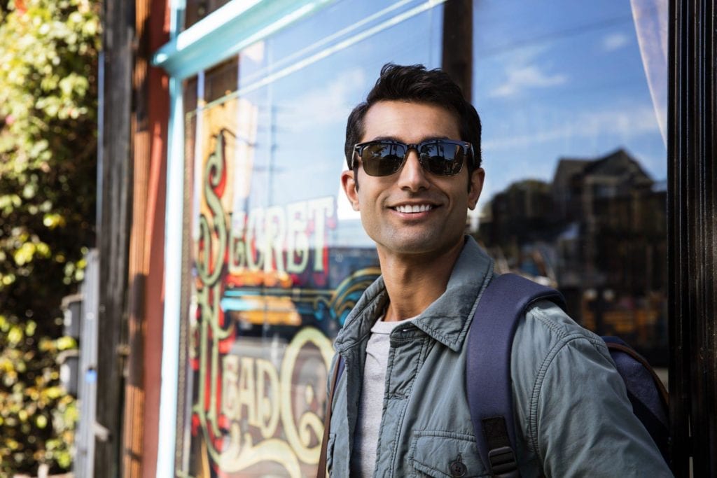 Smiling young man outside a cafe wearing sunglasses and Invisalign clear aligners Highland Park